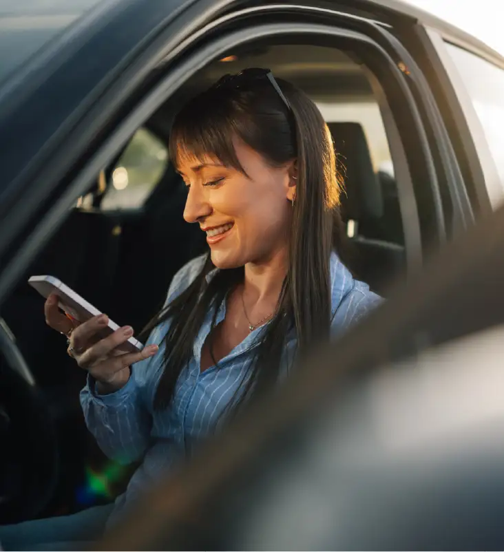 Woman sitting in her car finding car insurance quotes on her mobile phone